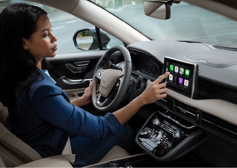 A woman in the driver’s seat of a 2022 Lincoln Corsair is touching the center digital screen to connect to Apple CarPlay<sup>®</sup> | Empire Lincoln in Abingdon VA