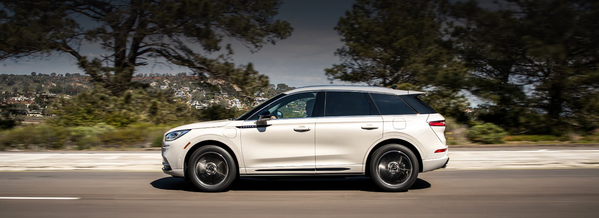 A 2021 Lincoln Corsair Grand Touring in Pristine White is being driven on a freeway as blue skies and sunlit trees grace the edges of the road