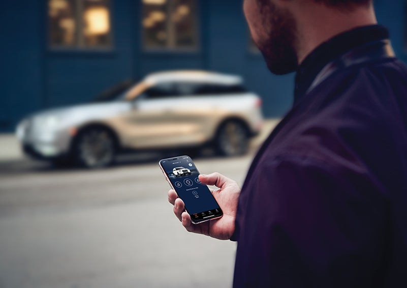 A person is shown interacting with a smartphone to connect to a Lincoln vehicle across the street. | Empire Lincoln in Abingdon VA