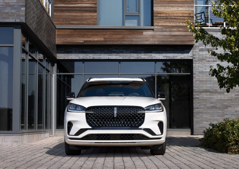 A white 2025 Lincoln Aviator® SUV is shown parked outside a modern building with gray brick and wood accents. | Empire Lincoln in Abingdon VA