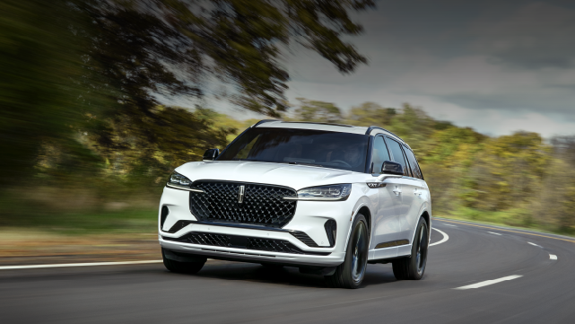 A white 2025 Lincoln Aviator® SUV is being driven down a road lined with trees. | Empire Lincoln in Abingdon VA