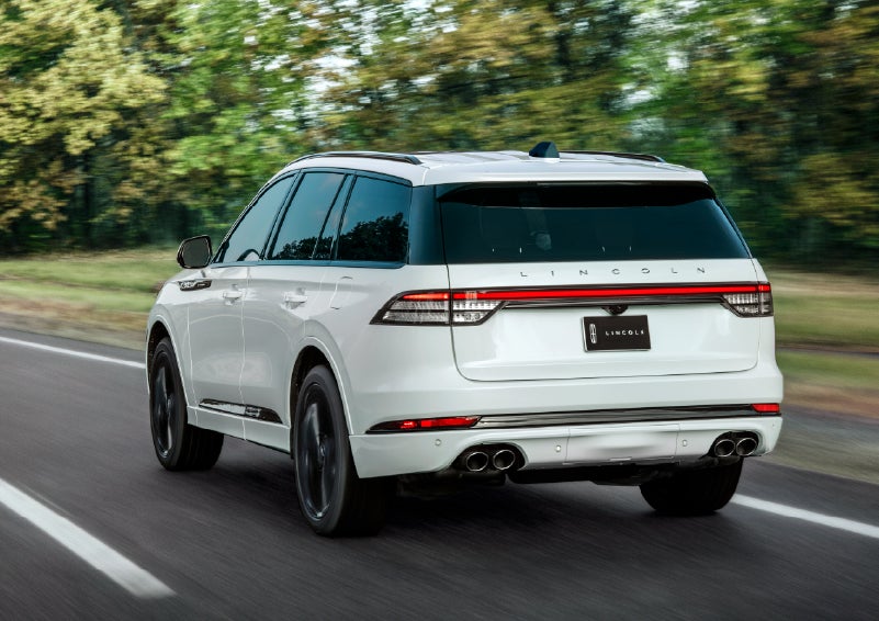 A white 2026 Lincoln Aviator® SUV is being driven away down a road lined with colorful trees. | Empire Lincoln in Abingdon VA