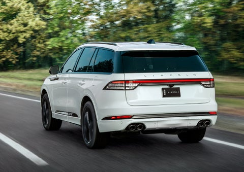 A white 2026 Lincoln Aviator® SUV is being driven away down a road lined with colorful trees. | Empire Lincoln in Abingdon VA