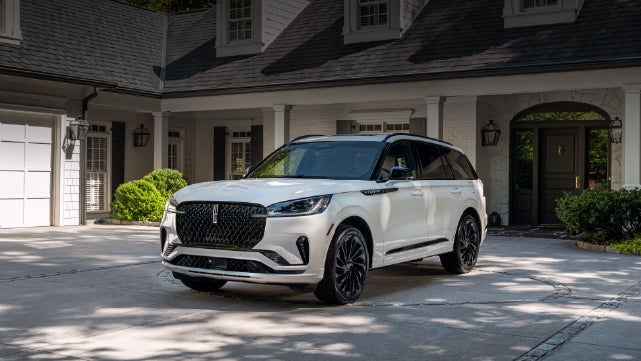 A white 2026 Lincoln Aviator® SUV is parked in the driveway of a luxury home. | Empire Lincoln in Abingdon VA